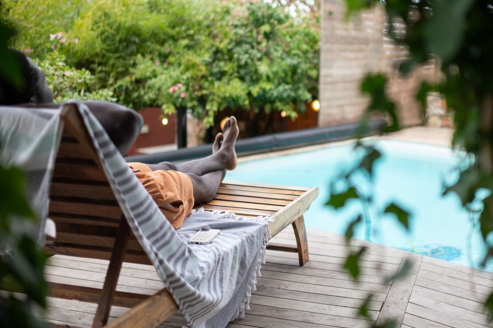 Feet up on a lounger by the pool, framed in leaves